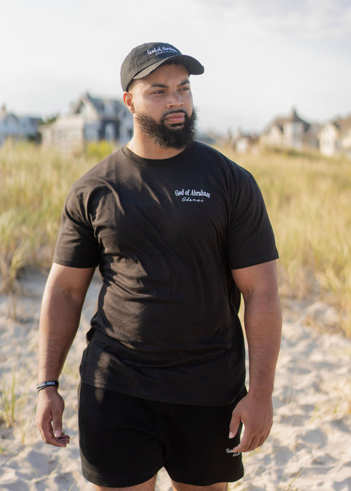 Man wearing a black God of Abraham Adoani t-shirt and matching cap on a beach